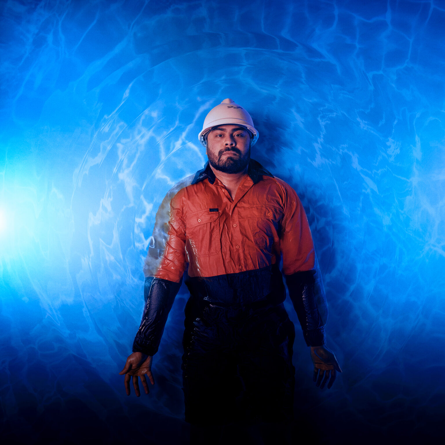 Man floating in blue glowing pool wearing orange reflective trade outfit and construction helmet